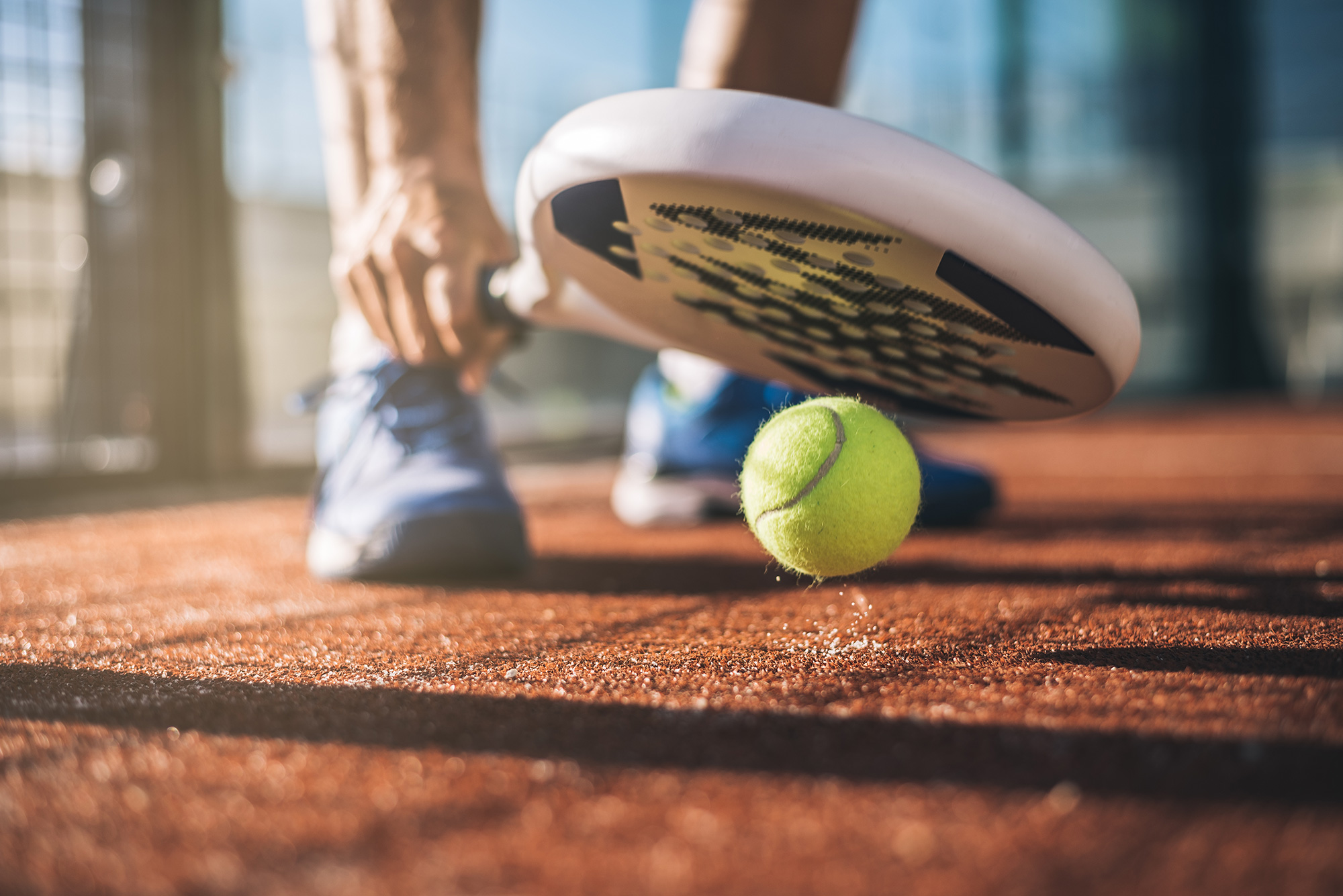 Someone picking a ball up off the floor with their padel racket